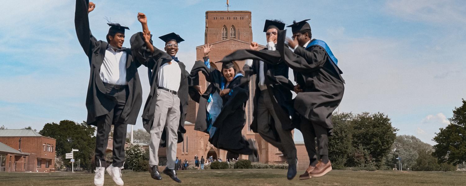 A group of students in graduation outfits jumping in front of the Cathedral