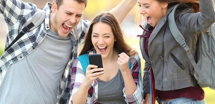 Three students are joyfully laughing and holding their mobile phones