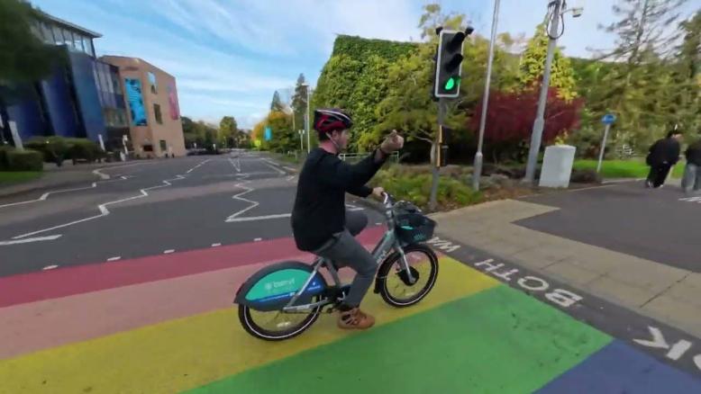 A student on a Beryl Bike is crossing the road while making a thumbs up